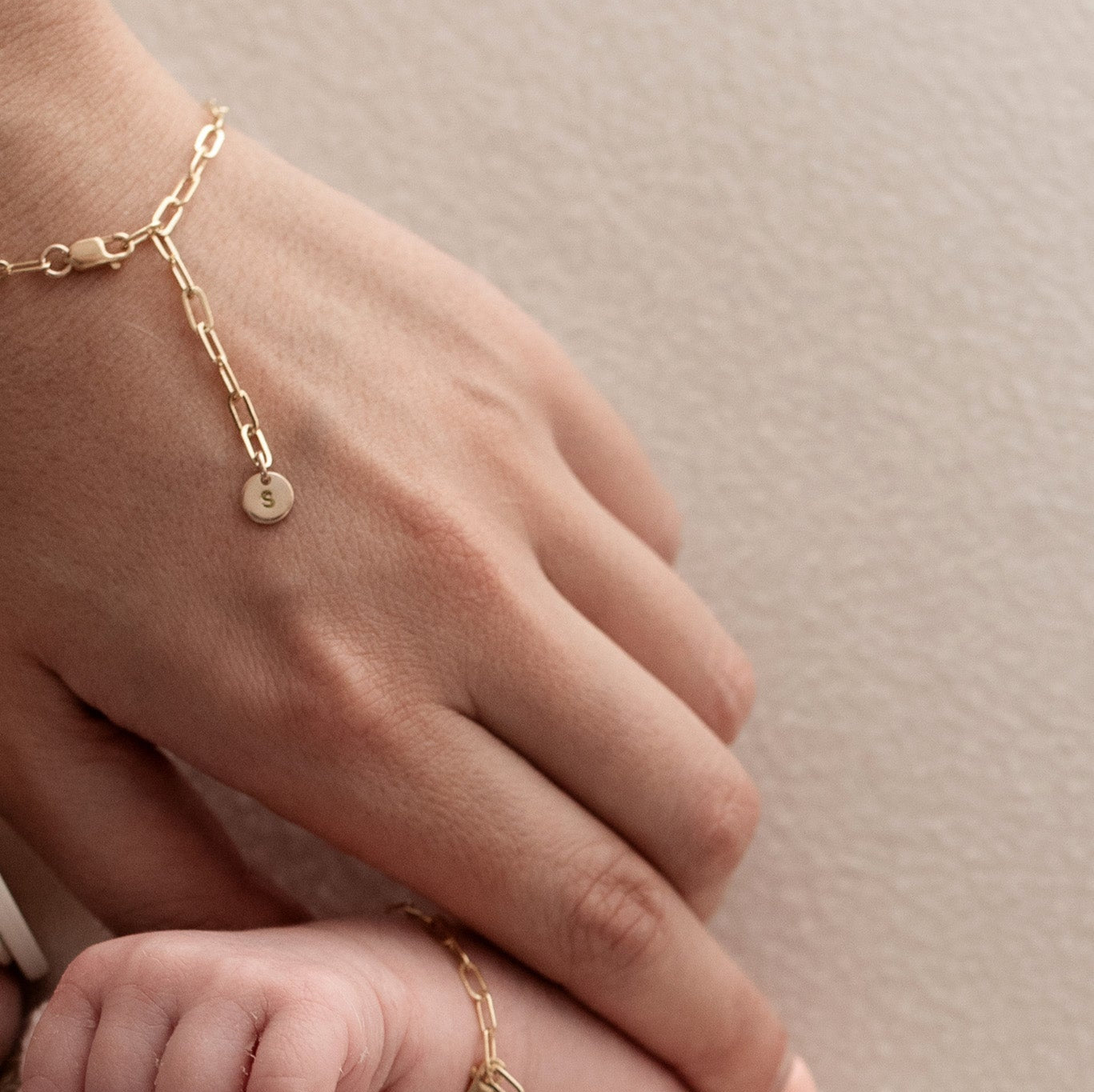 Close-up of hands wearing gold bracelets on a neutral background