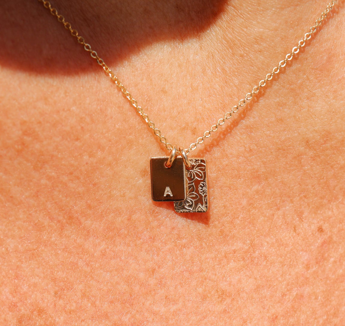Gold necklace with a square pendant featuring an 'A' on a person's neck.