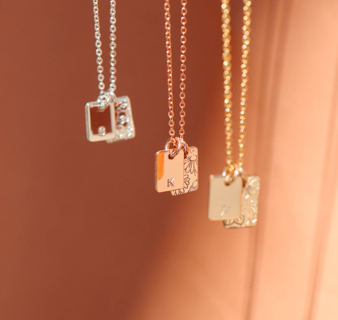 Three necklaces with square pendants on a soft pink background