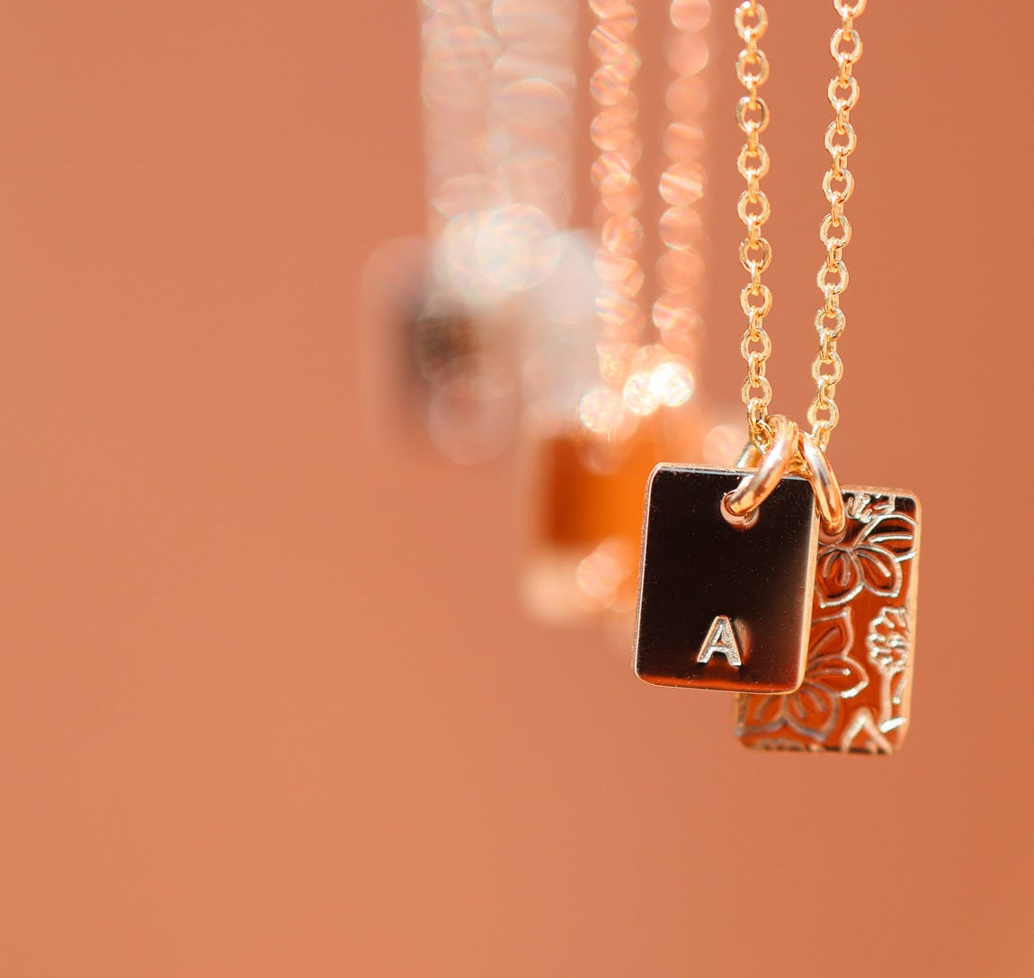 Gold necklace with a square pendant featuring the letter 'A' on a blurred background