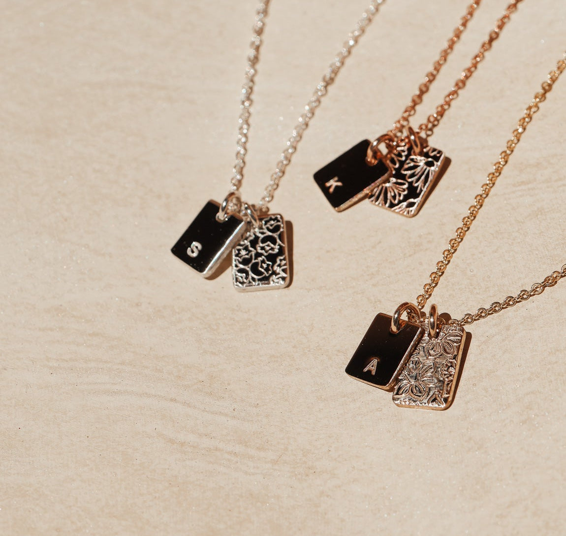 Three necklaces with rectangular pendants on a beige surface