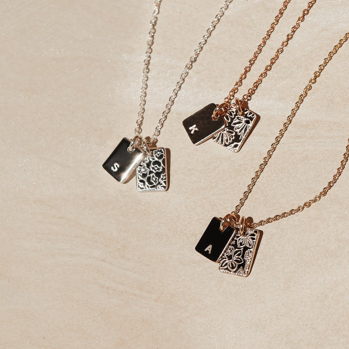 Three gold necklaces with rectangular pendants on a beige background