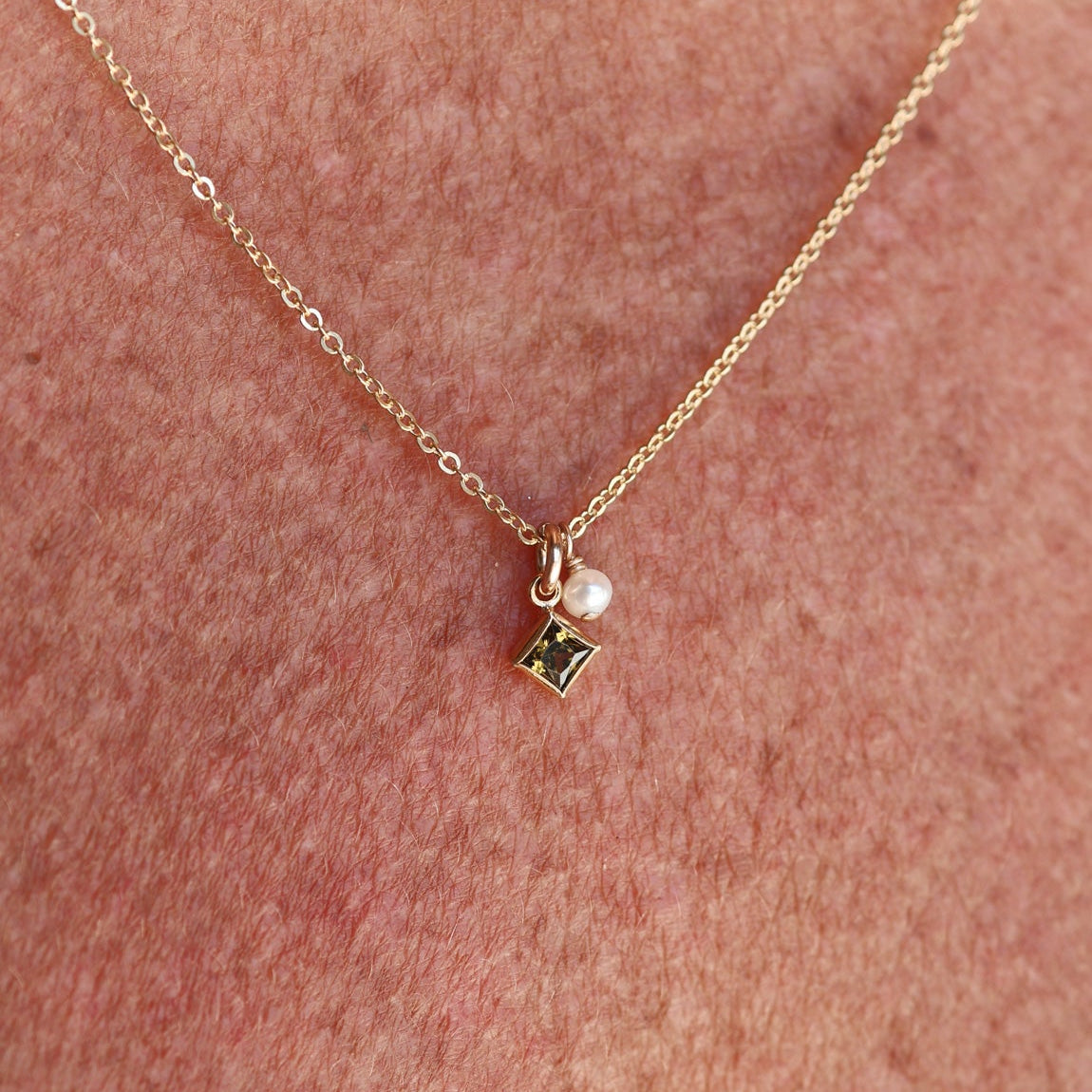Gold necklace with a small pendant on a person's neck against a pinkish-brown background - Birthstone Necklace - ting pearl necklace