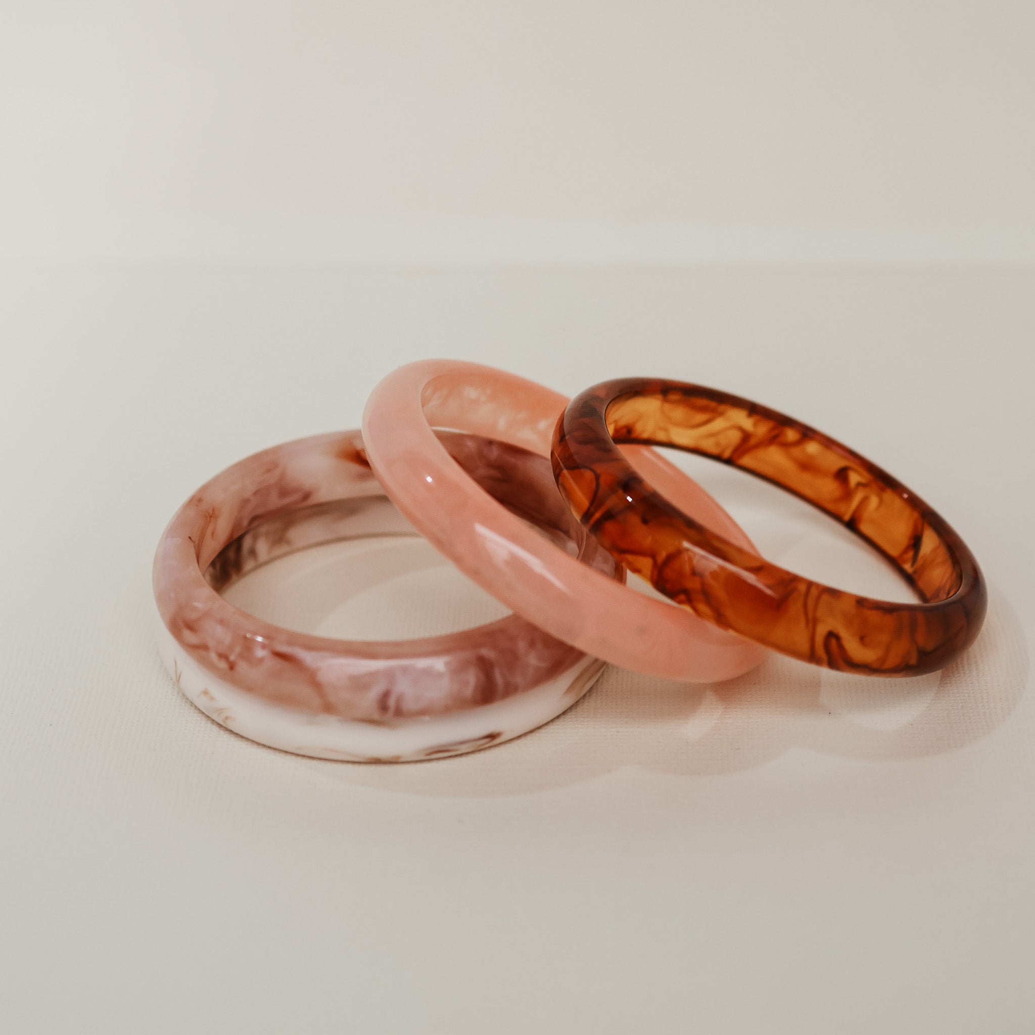 Three translucent bangles in pink, clear, and brown on a light beige background - KBN RESIN BANGLES