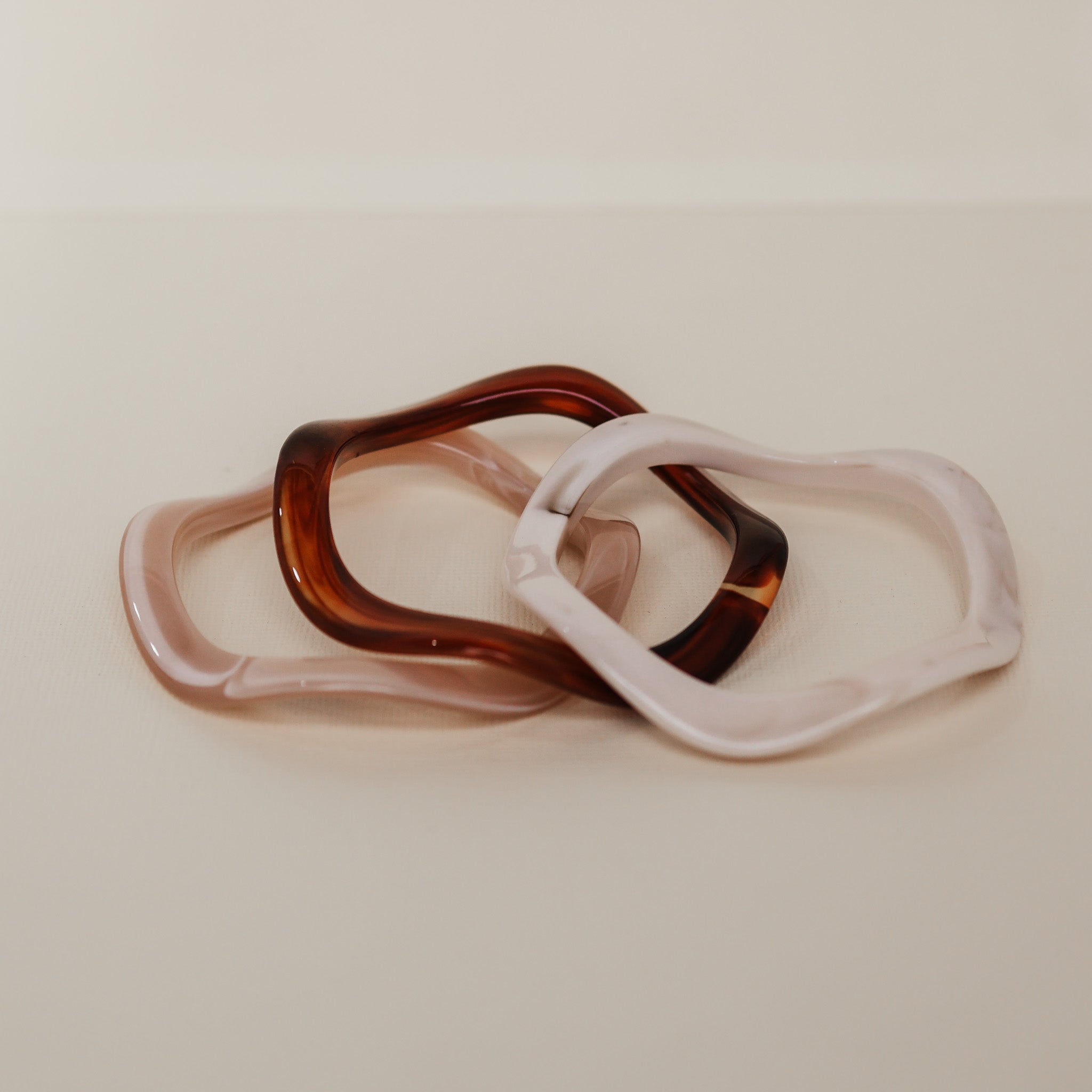 Two pairs of sunglasses with tortoiseshell and clear frames on a beige background - KBN RESIN BANGLES