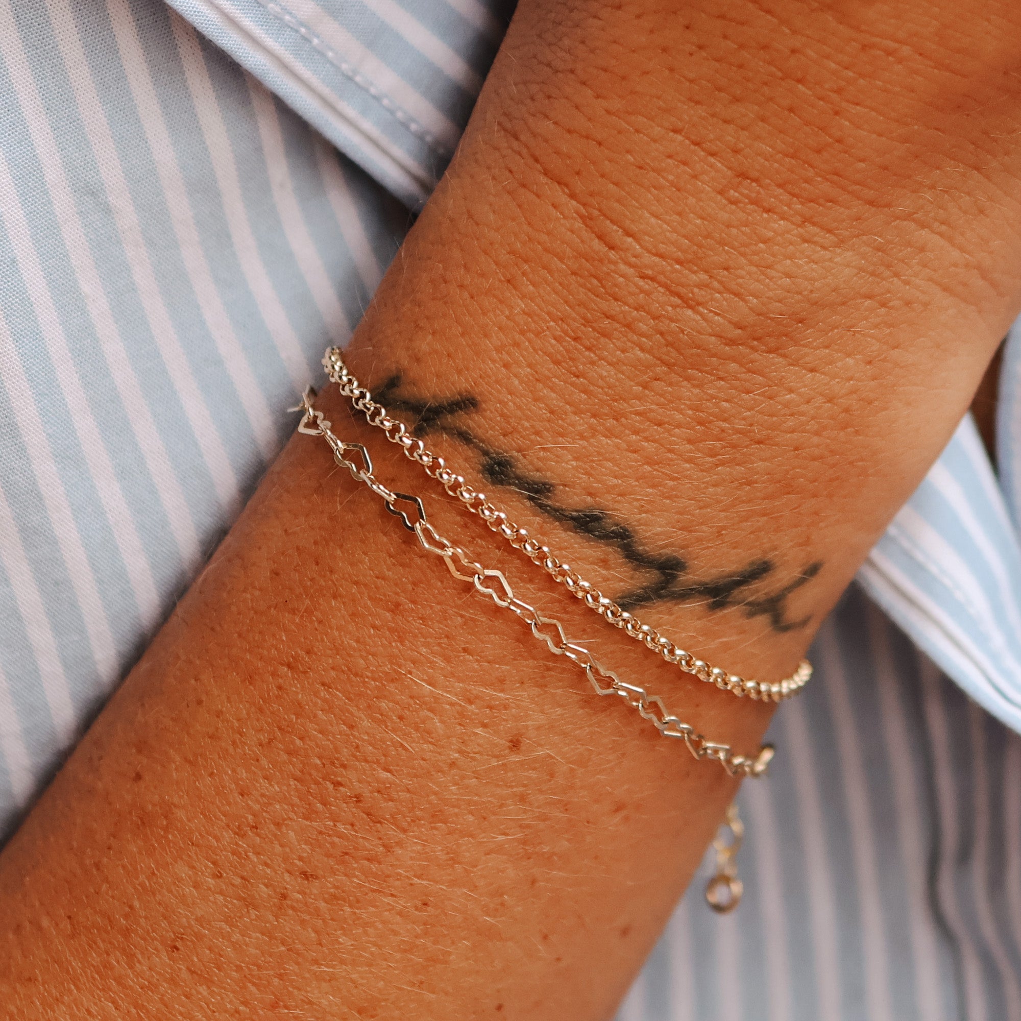 rolo bracelet, stacked bracelet worn, Stacked bracelet look – A wrist adorned with multiple bracelets, featuring the rolo chain bracelet and a heart chain bracelet