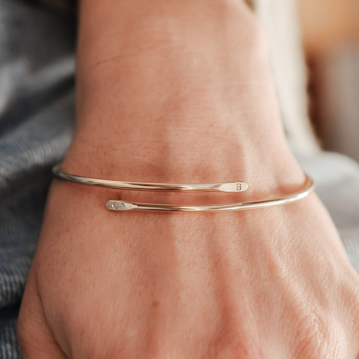 Close-up of a hand wearing a gold initial bracelet and ring on a blurred background