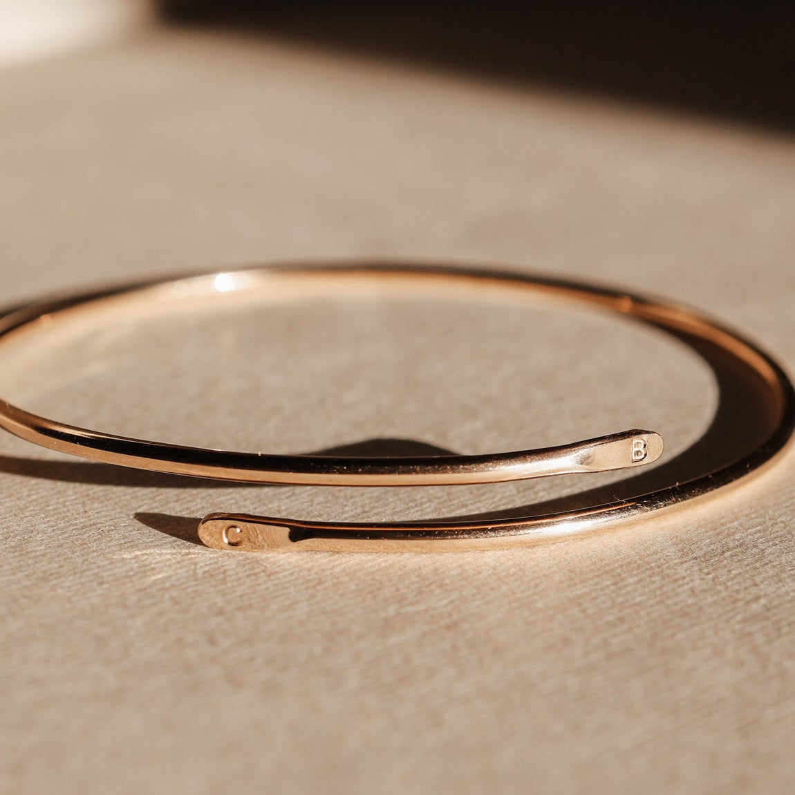 Gold initial bangle bracelet on a textured beige surface