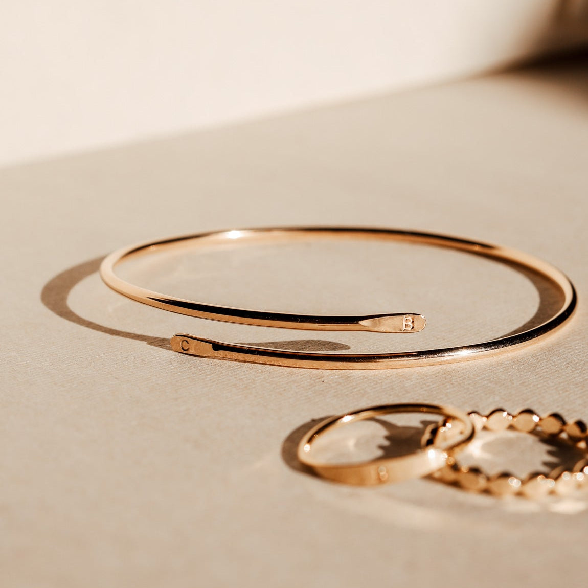 Gold bracelet and ring on a beige surface
