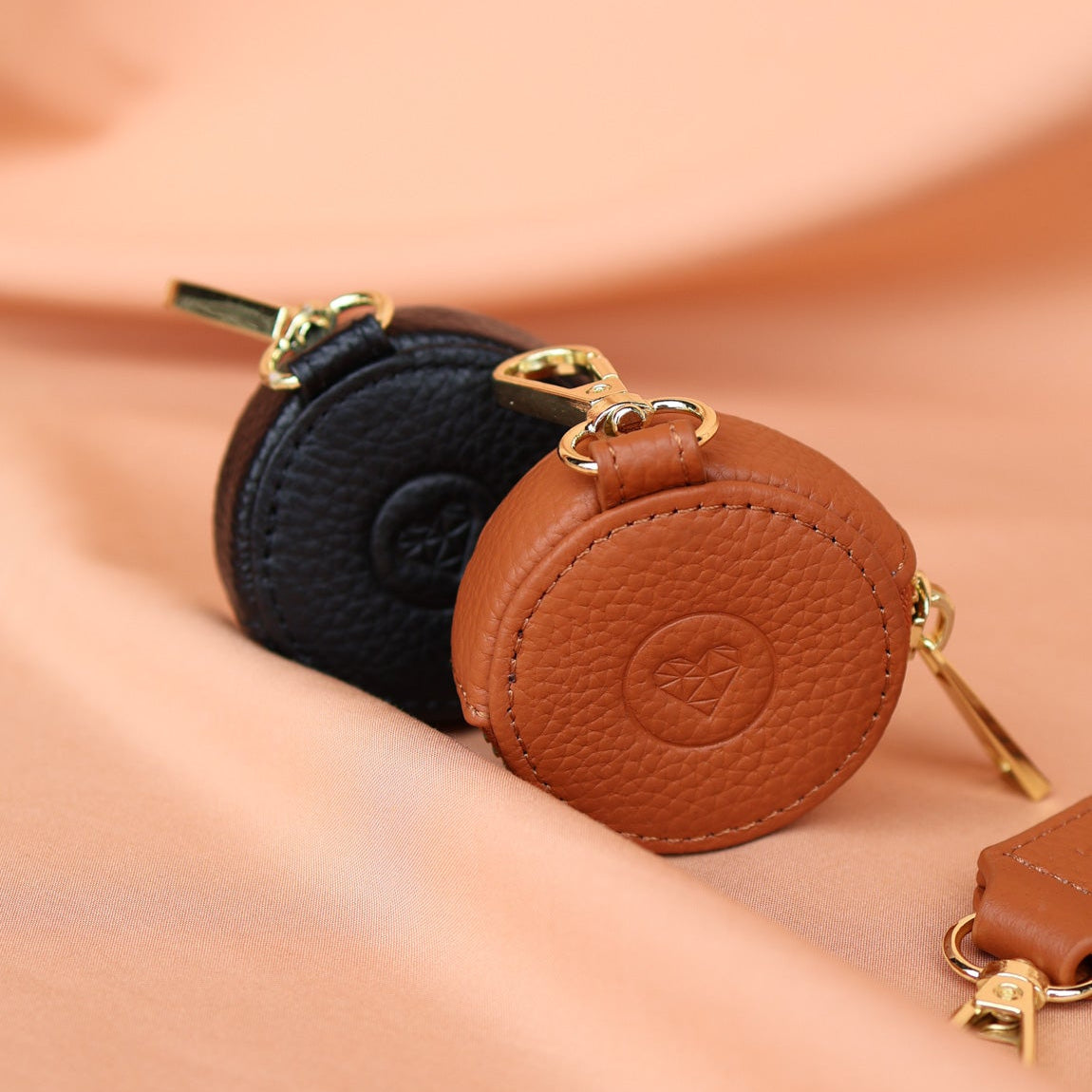 Three round leather coin purses in black, brown, and gold on a beige background