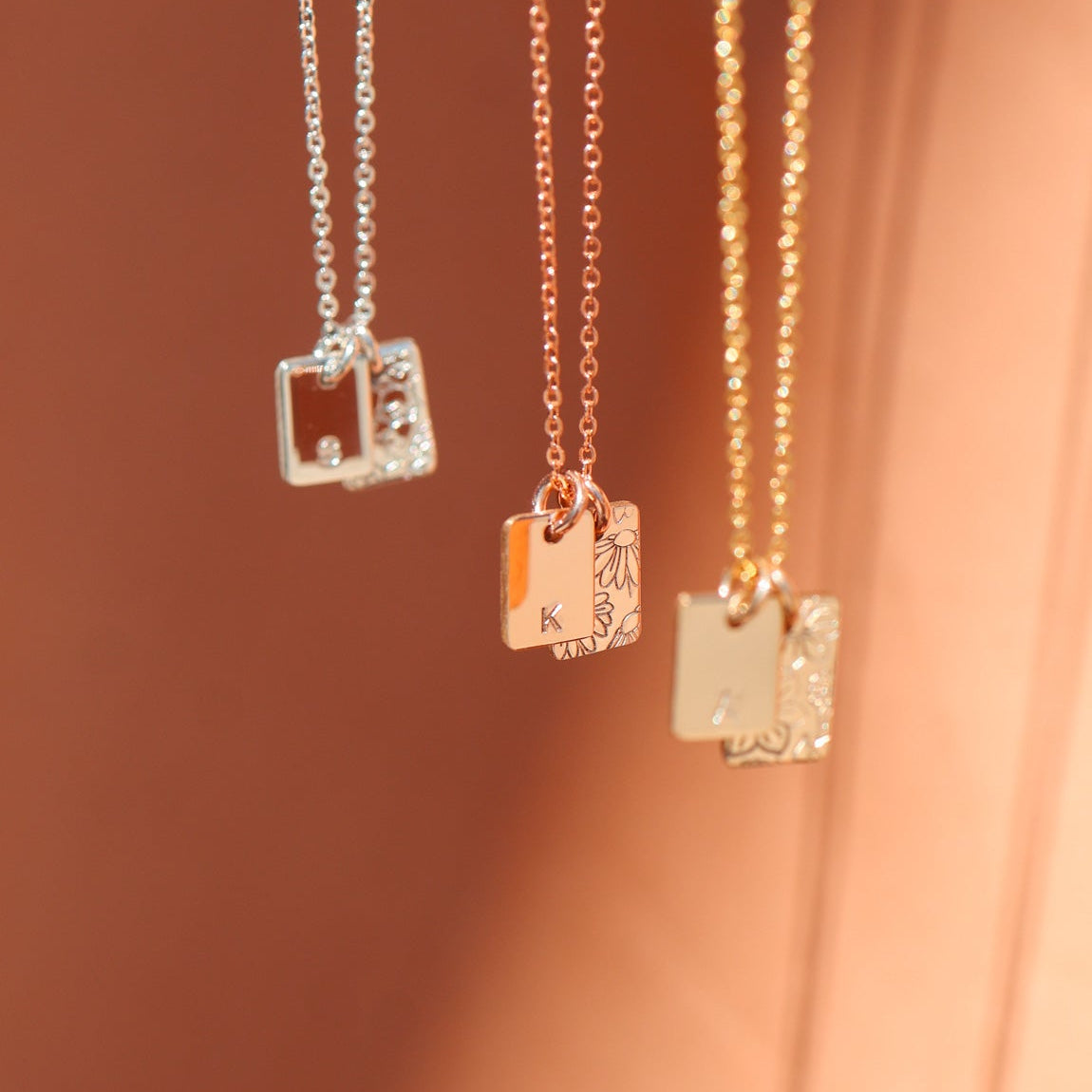 Three necklaces with square pendants on a soft pink background