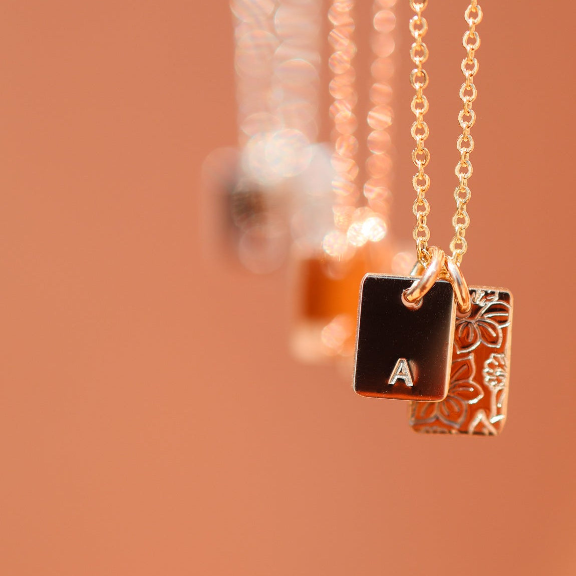 Gold necklace with a square pendant featuring the letter 'A' on a blurred background