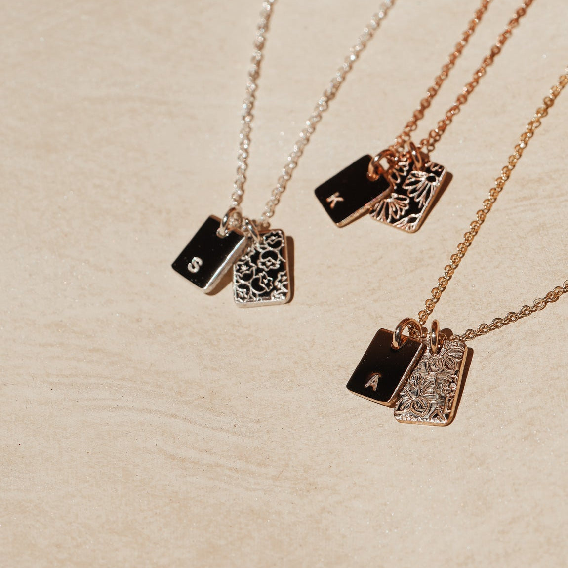Three necklaces with rectangular pendants on a beige surface