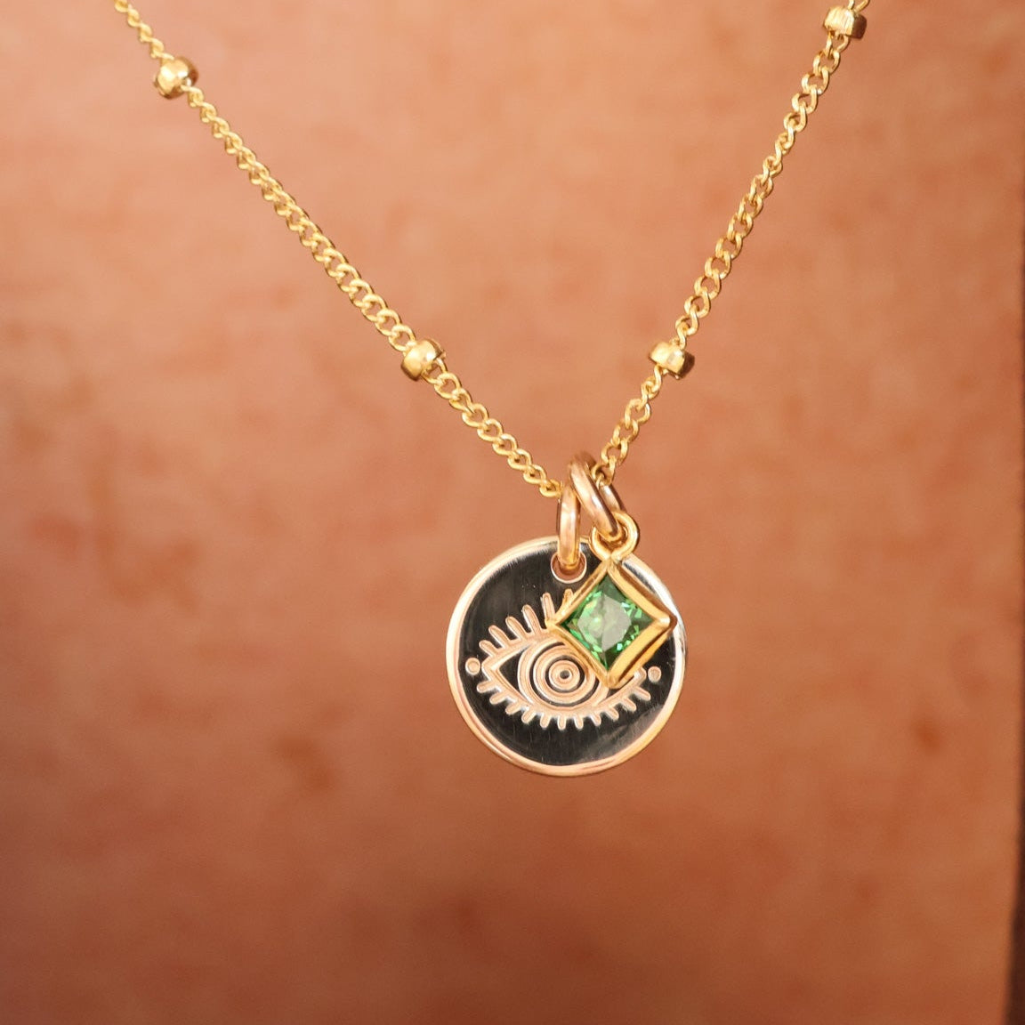 delicate gold satelite chain necklace with small evil eye pendant and a small square green birthstone accent. Brisbane personalised jewellery