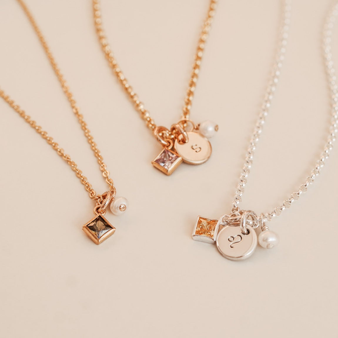 Three gold necklaces with various charms on a beige background KBN Jewellery -  birthstone necklace - initial tiny pendant necklace