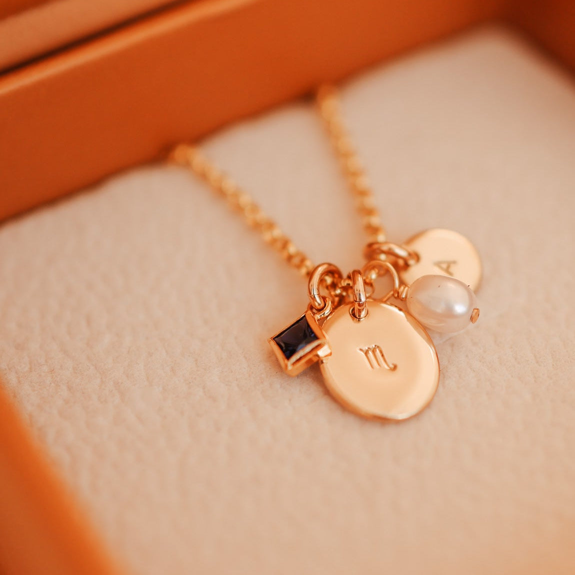 Gold necklace with charms on a soft orange surface - KBN Jewellery Cluster Necklace - birthstone, initial & pearl necklace