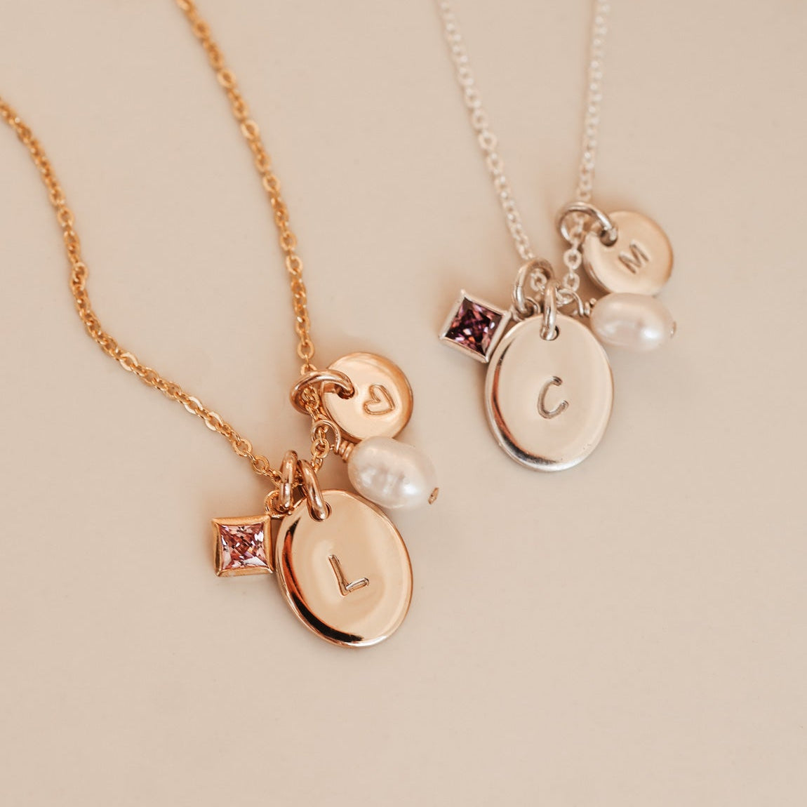 Two gold necklaces with charms on a beige background
