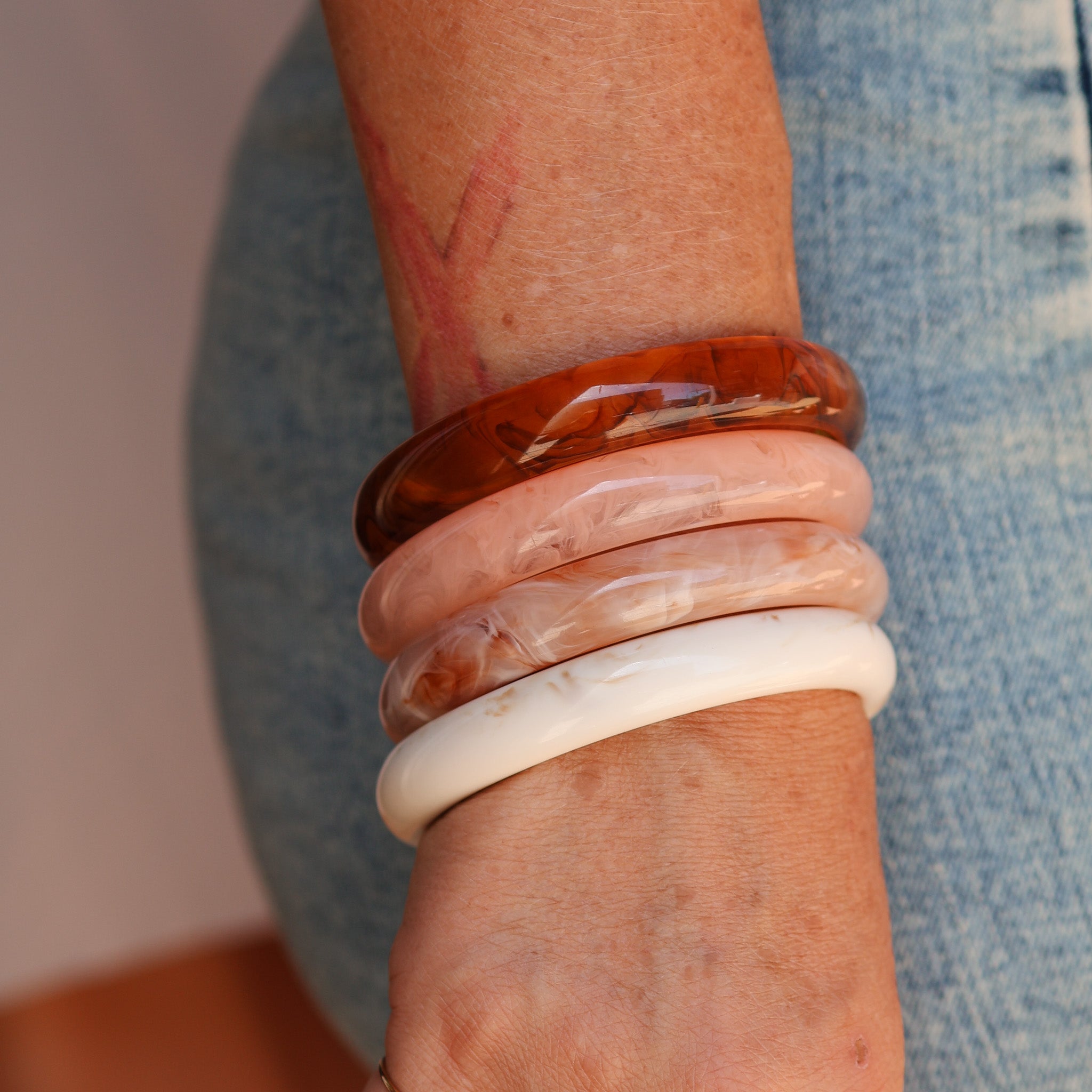 Close-up of a wrist wearing multiple translucent bracelets on a blurred background - KBN RESIN BANGLES