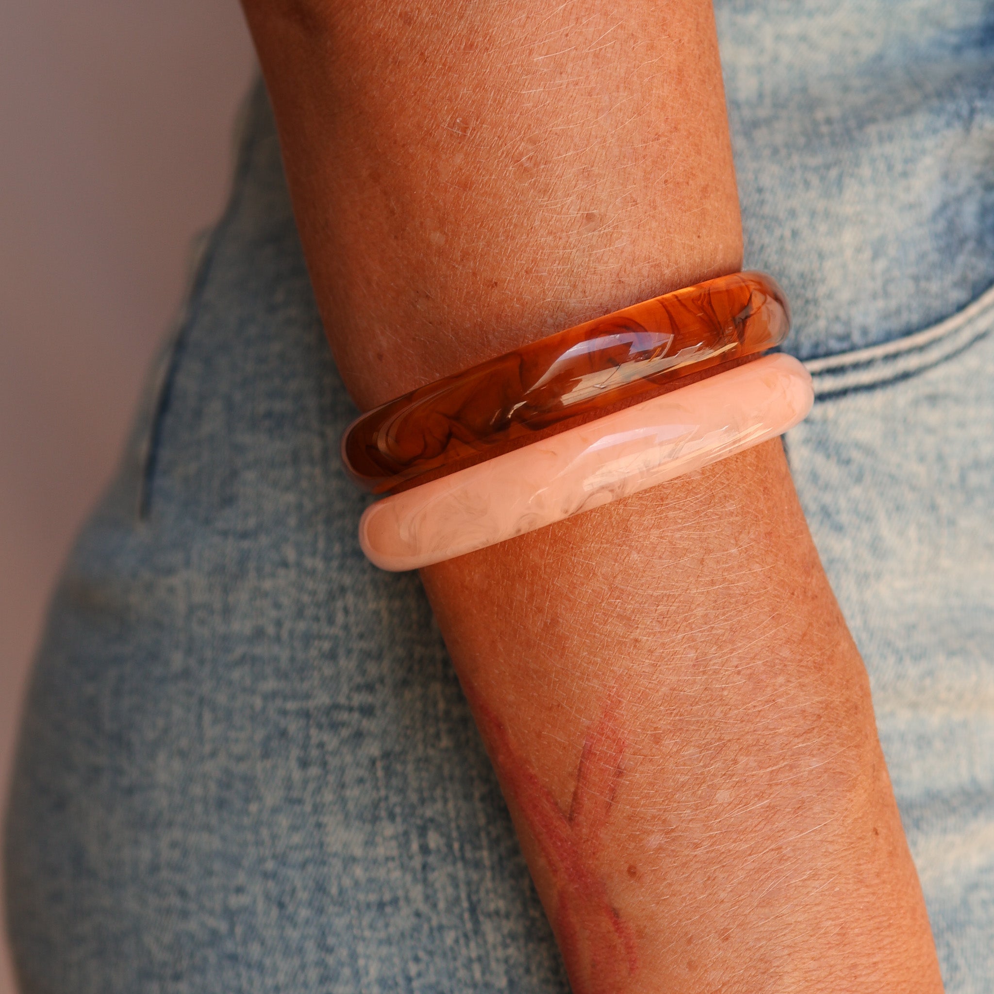Close-up of a person's arm wearing a transparent bracelet with a pink band. - KBN RESIN BANGLES